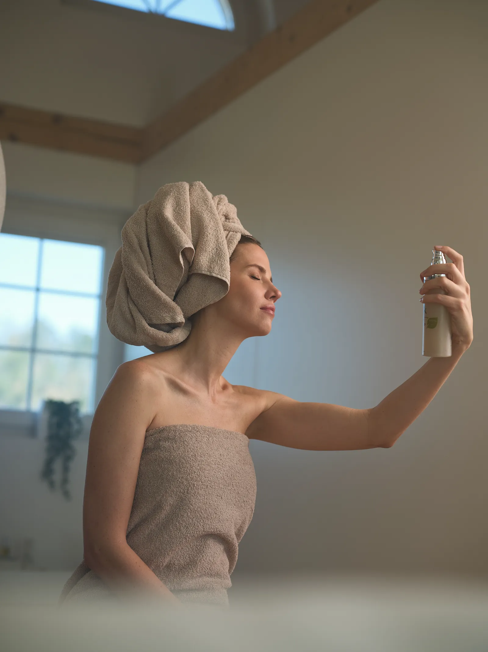 Model im Handtuch sprüht sich Toner als feinen Nebel ins Gesicht