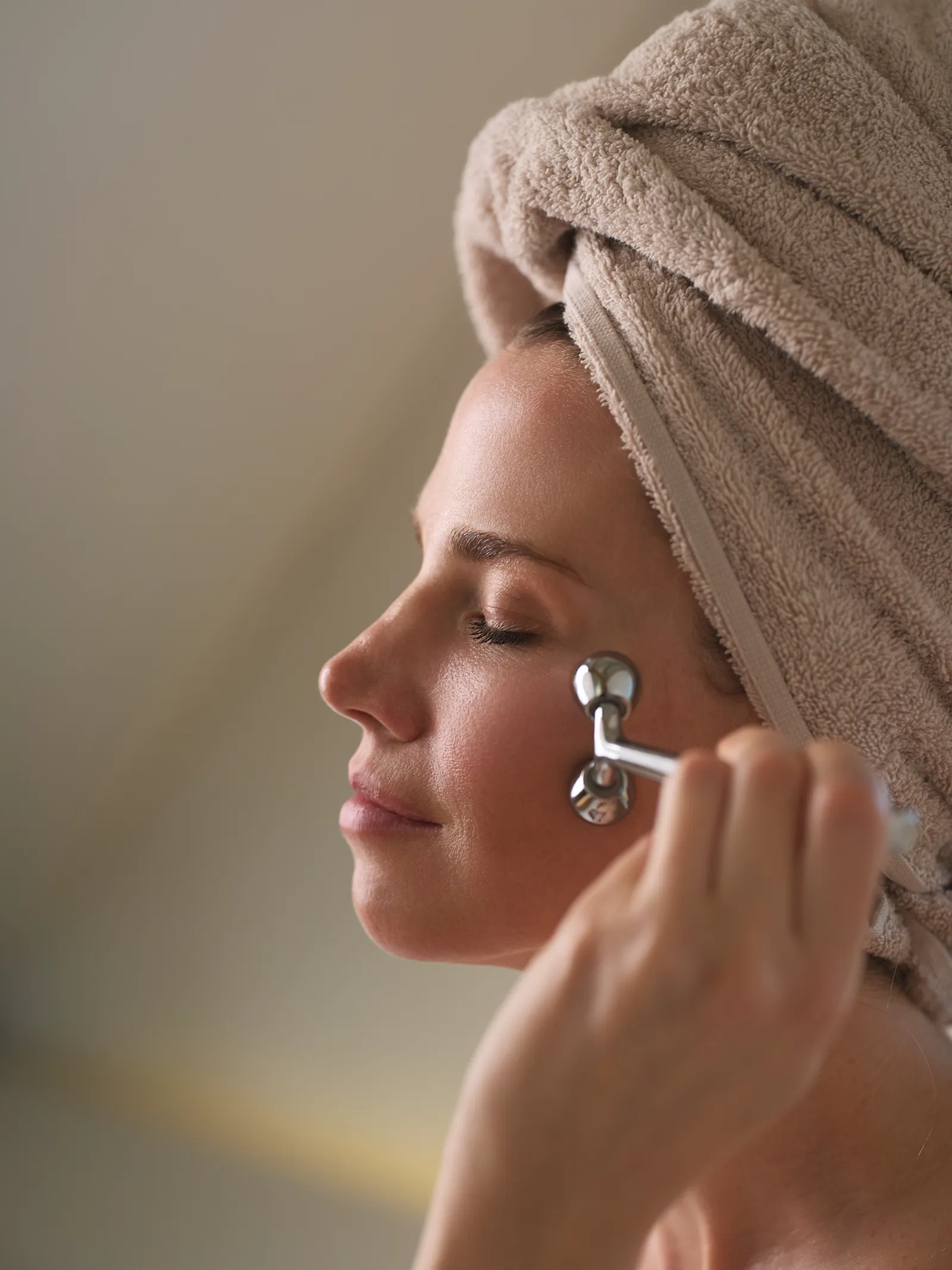 Model mit Handtuchturban nutzt einen silbernen Gesichtsroller an der Wange